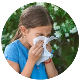 A young girl outside, sneezing into a tissue
